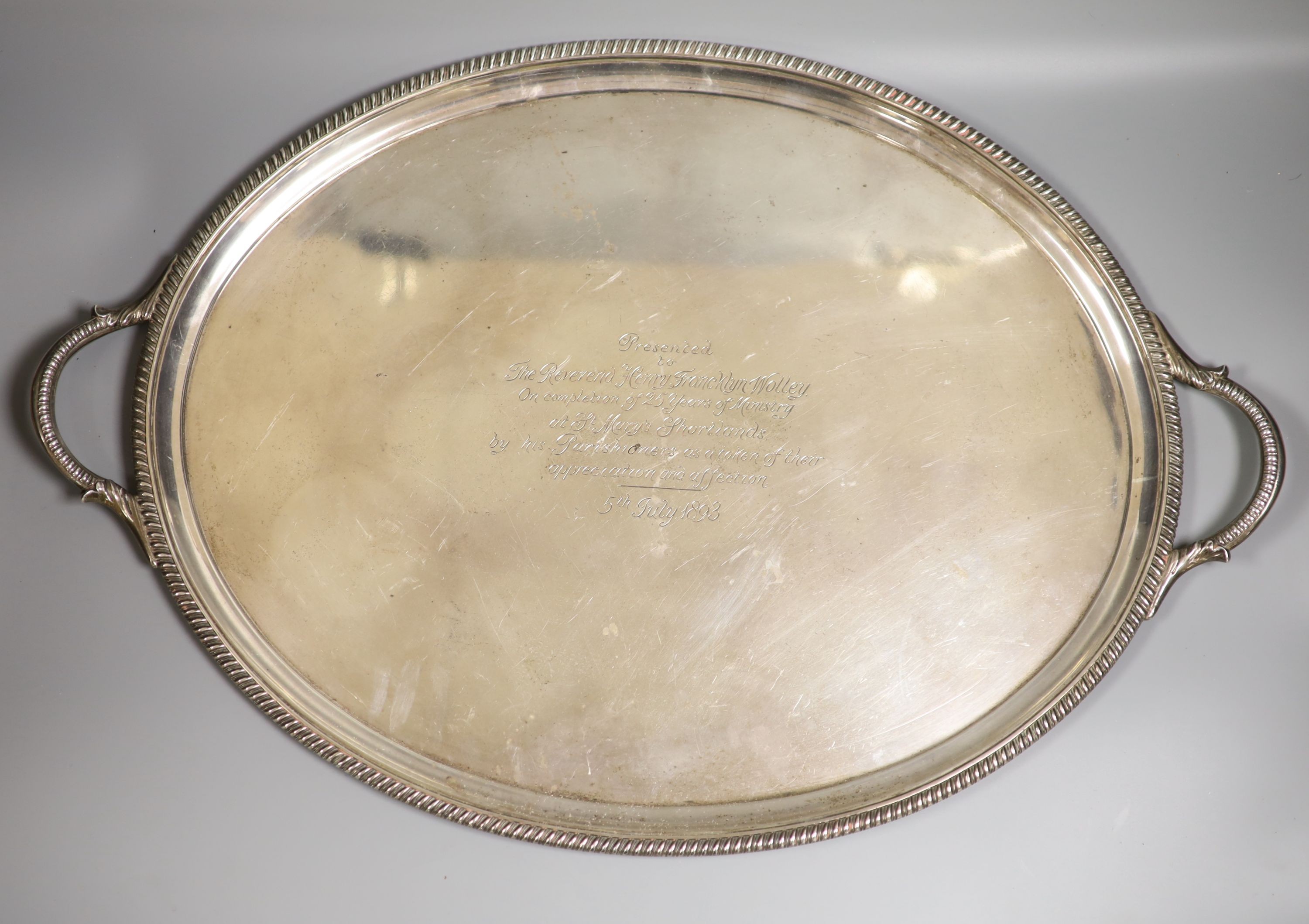 A late Victorian silver oval two handled tea tray, with gadrooned border and engraved inscription, George Gilliam, London, 1893, 62.8cm over handles, 99oz.